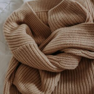 Home A close-up shot of a cozy, beige knitted sweater on a soft bedspread, perfect for winter fashion.