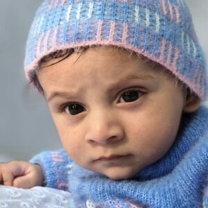 Home Charming baby wearing a knitted blue hat and sweater, exuding warmth and cuteness.