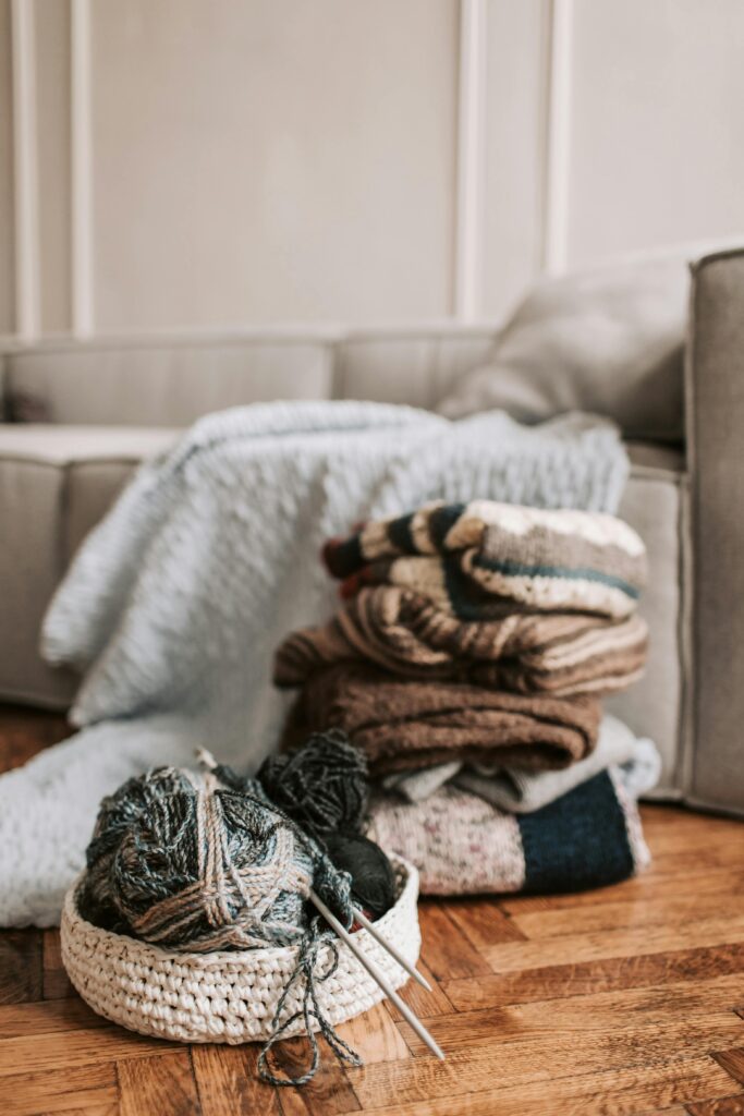 A collection of knitted sweaters and yarn arranged on a wooden floor, creating a warm and inviting atmosphere.