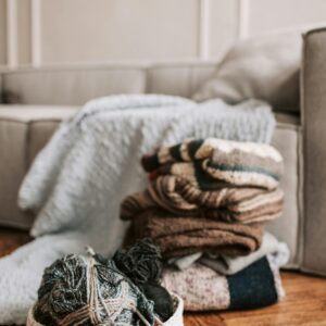 Home A collection of knitted sweaters and yarn arranged on a wooden floor, creating a warm and inviting atmosphere.