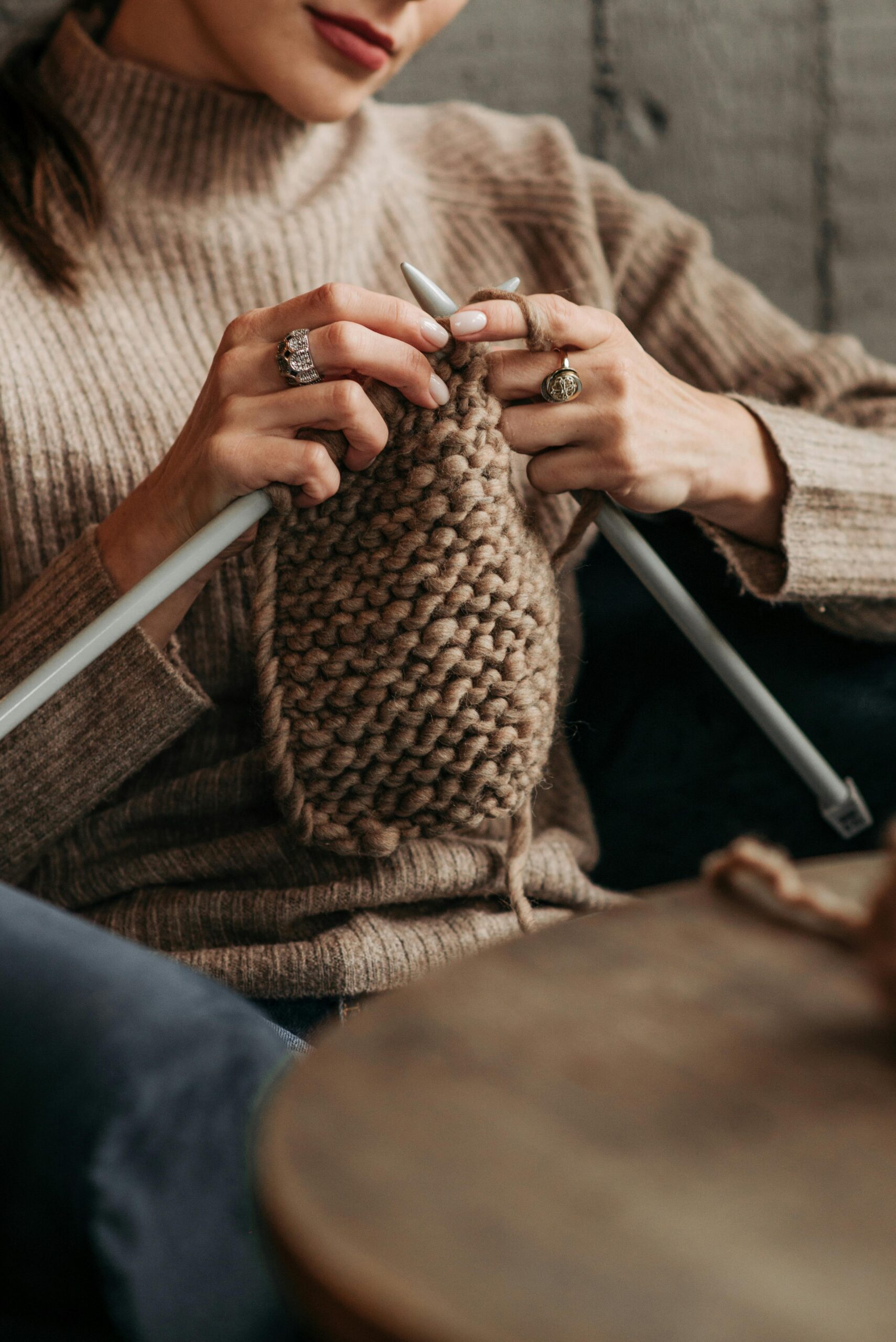 A woman knitting with brown wool yarn indoors, showcasing craftsmanship and relaxation.