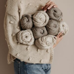 Stylish woman in a knitted sweater holding yarn balls for crafting projects.